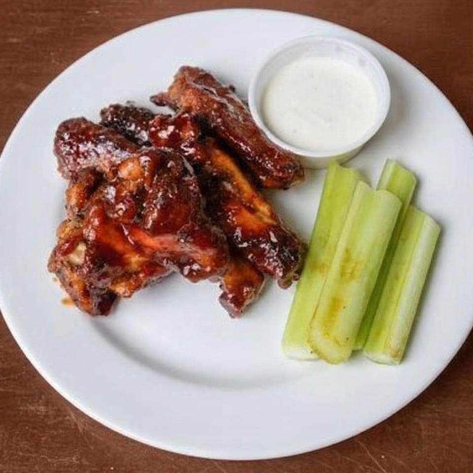 A plate of BBQ chicken wings with a side of celery sticks and ranch dipping sauce.