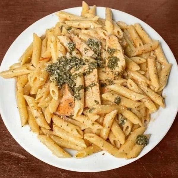Penne pasta with creamy sauce, chicken, and pesto on a white plate.