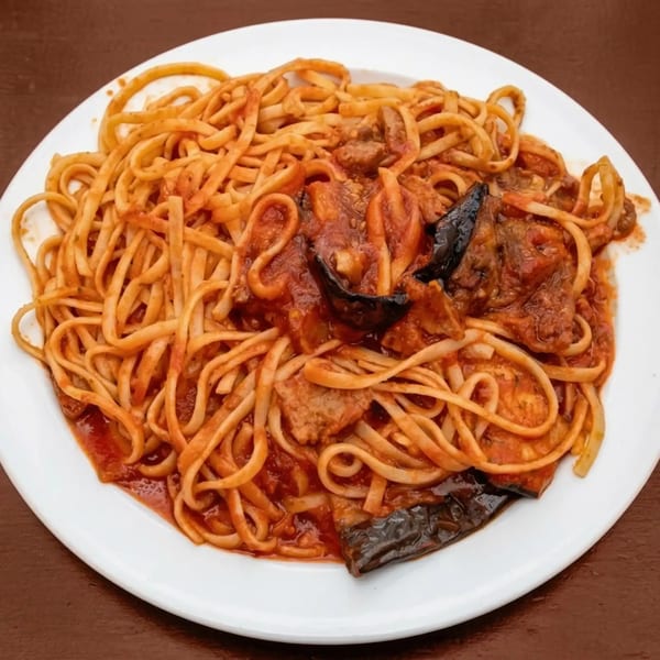 A white plate filled with linguine pasta, red sauce, meat, and dark eggplant slices.