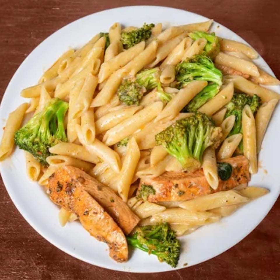 Penne pasta with broccoli and chicken pieces in a creamy sauce on a white plate.