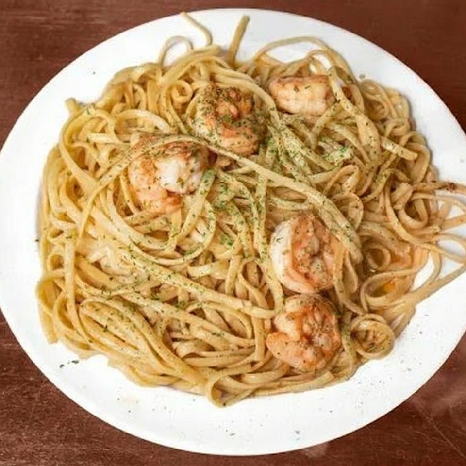 A white plate holds linguine pasta with shrimp and green herbs, on a brown surface.