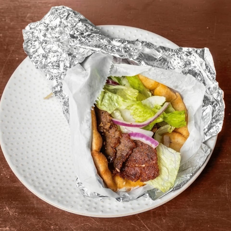 A gyro with meat, lettuce, red onion, and fries, wrapped in paper and foil on a white plate.