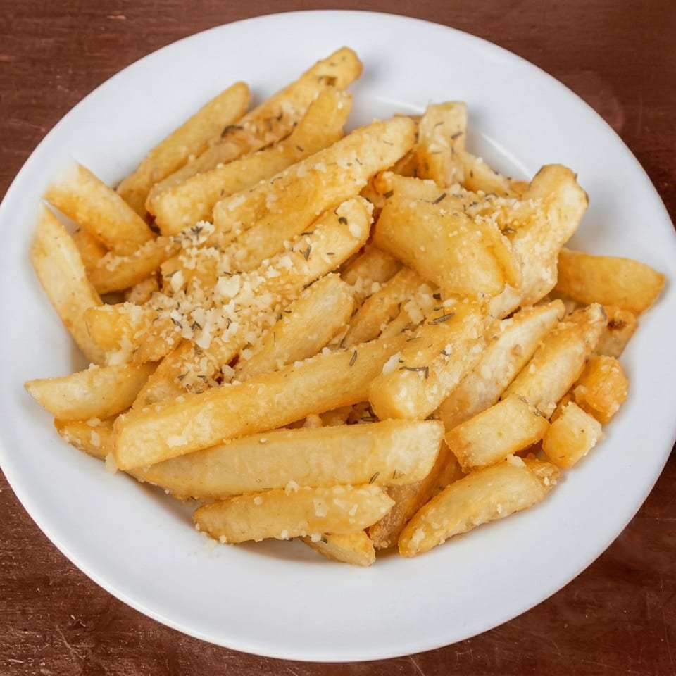 A white plate filled with golden french fries, sprinkled with herbs and grated cheese.