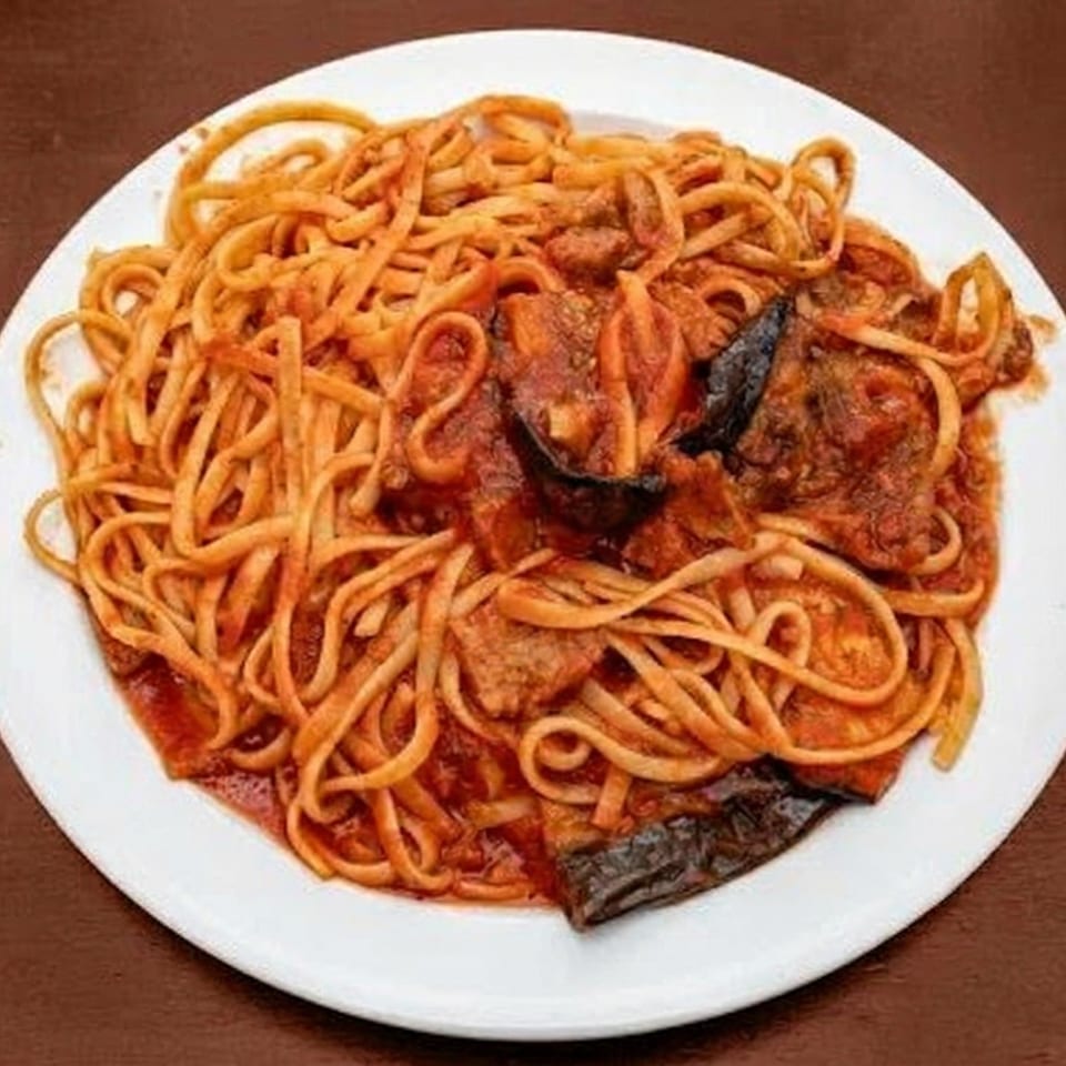 A white plate holds a serving of linguine pasta with red sauce and pieces of eggplant.